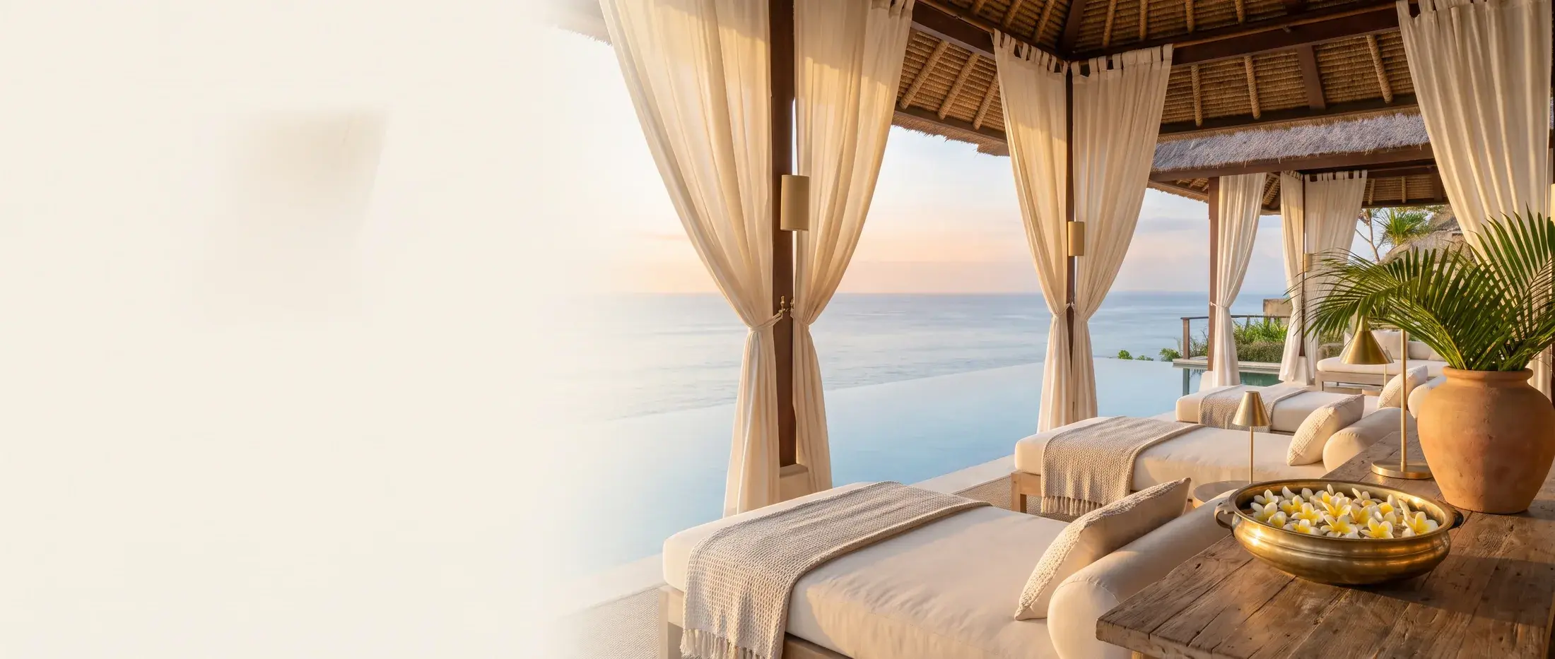 An open-air wellness pavilion over the Indian Ocean at dawn, with linen daybeds and a bowl of frangipani
